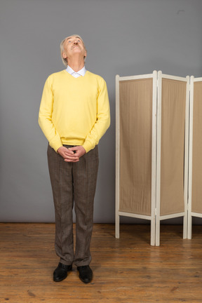 Front view of an old man looking up while holding hands together