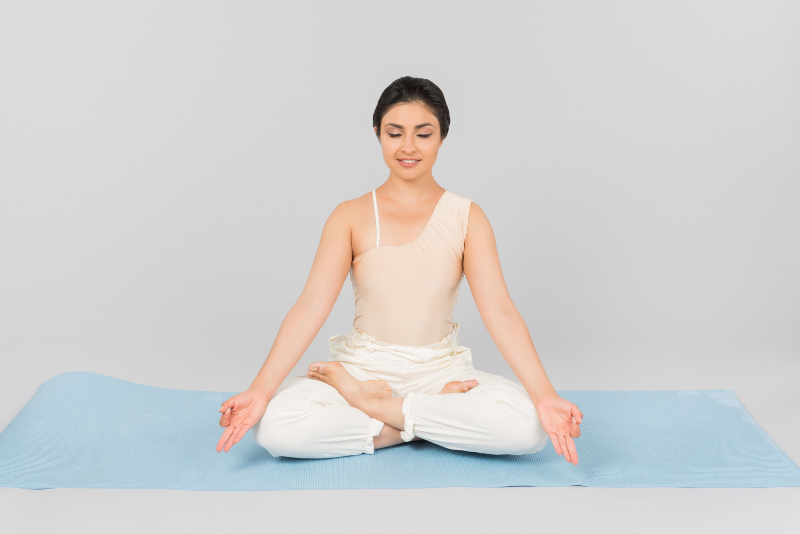 Young indian woman with legs crossed and hands extended sitting on yoga mat