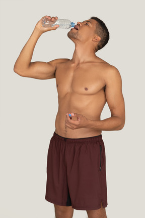 Bare chested young man in sport shorts drinking water