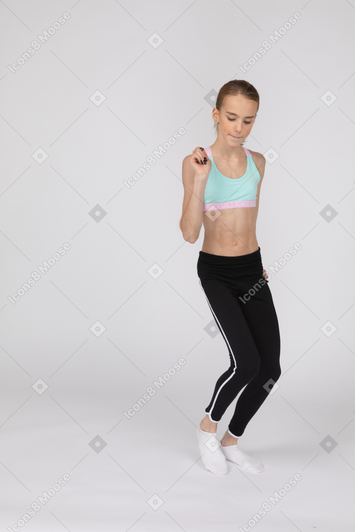 Front view of a teen girl in sportswear looking down and raising hand