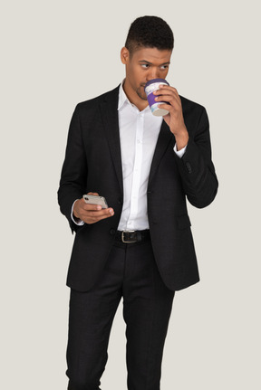 A good looking young guy dressed in black suit and drinking coffee