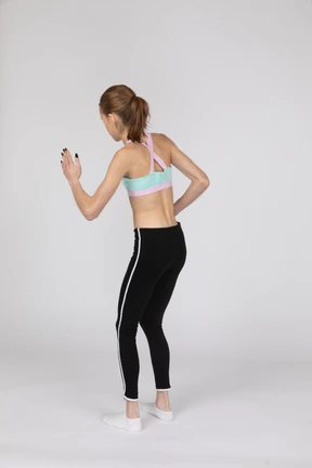 Vista posterior de tres cuartos de una adolescente en ropa deportiva inclinada hacia adelante mientras está de pie como un robot