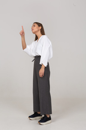 Vista de tres cuartos de una joven en ropa de oficina apuntando con el dedo hacia arriba