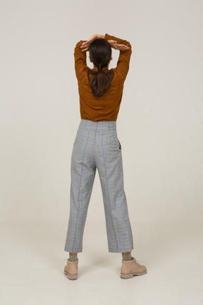 Vista traseira de uma jovem mulher asiática de calça e blusa, levantando as mãos