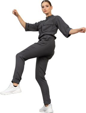 Side view of a young woman in a jumpsuit raising hands and leg