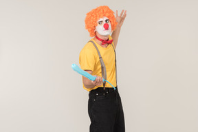 Male clown in red wig using balloon as a sword