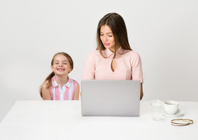 Hija sentada en la mesa mientras mamá trabaja en la computadora