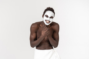 Um jovem negro com uma toalha de banho branca em torno de sua cintura indo sobre seu cuidado facial