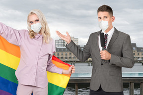 Reporter in face mask talking to a young woman in face mask with pride flag 