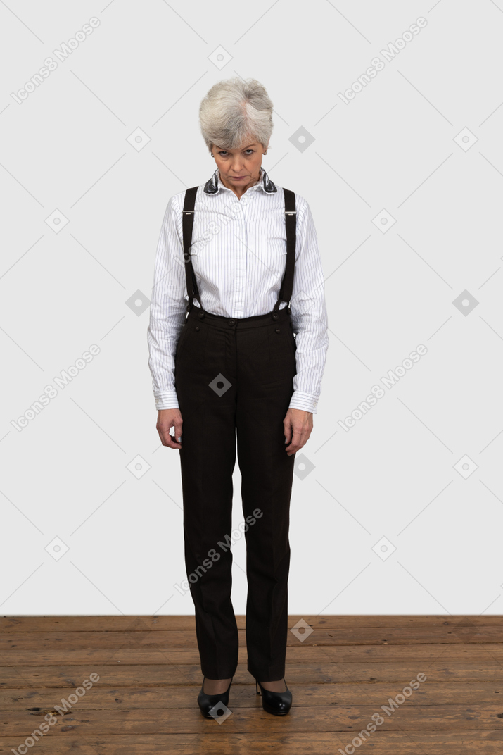 Front view of an old offended female in office clothes standing still indoors looking aside