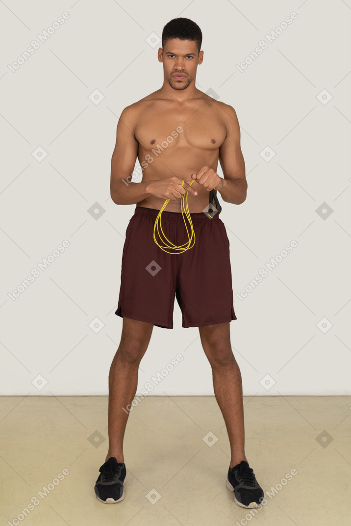 Bare chested young man in sport shorts standing with jumping rope over his neck