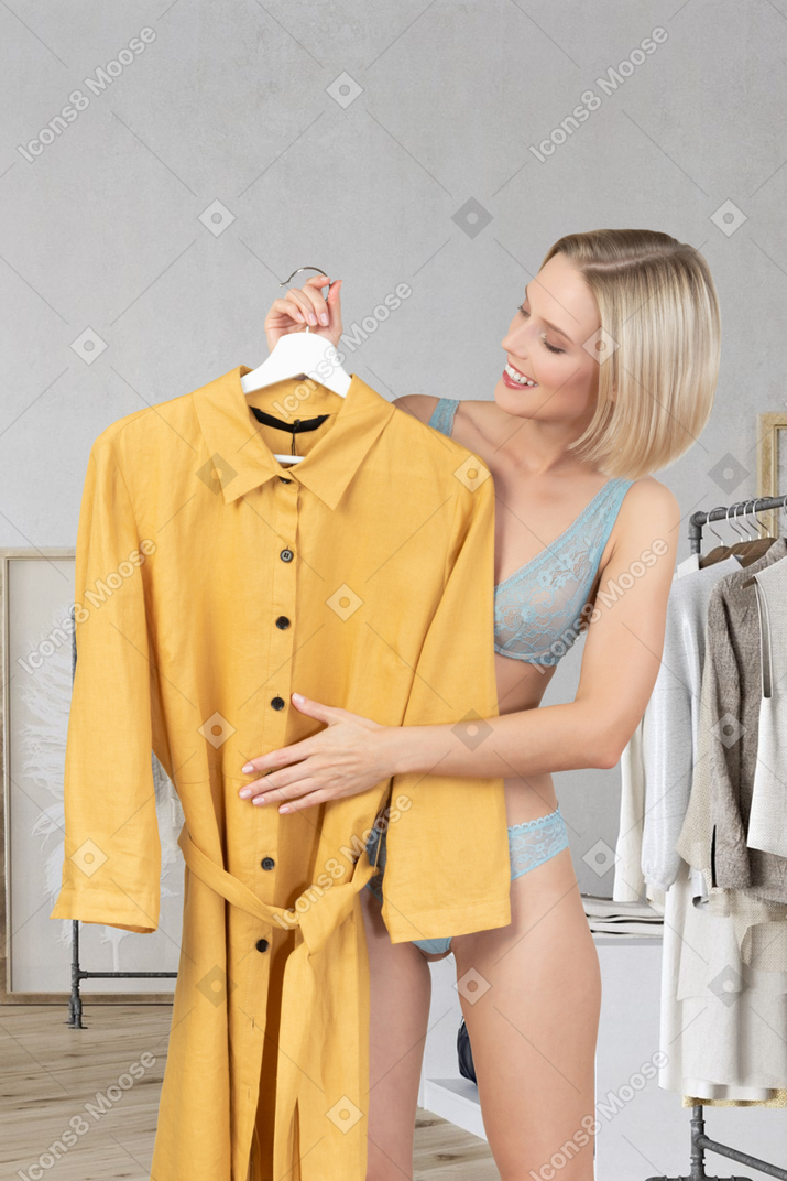 Frau in unterwäsche, die ein gelbes kleid hält