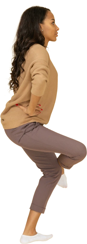 Side view of a dark-skinned young female raising leg & putting hands on hips