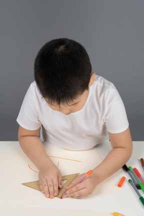 Garçon asiatique dessinant des formes géométriques à l'aide d'une règle triangulaire