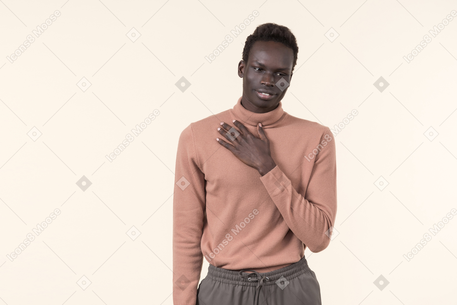 A young black man in a beige turtleneck and grey sweatpants standing casually on the white background
