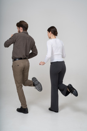 Vista posterior de tres cuartos de una pareja joven en ropa de oficina levantando la pierna