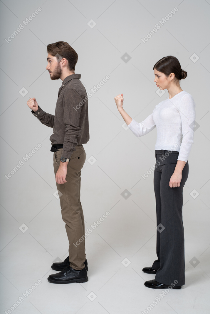 拳を示す事務服の厳格な若いカップルの側面図