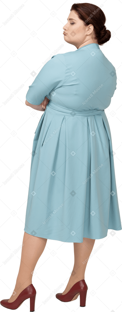 一个身穿蓝色连衣裙、双臂交叉站立的女人的后视图