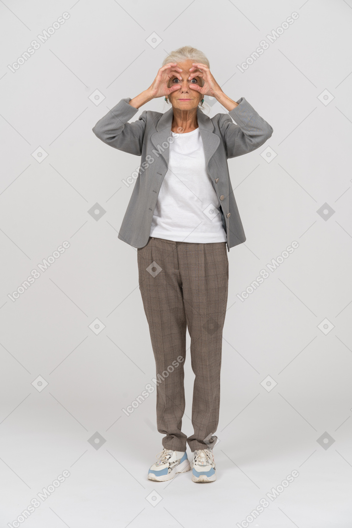 Vue de face d'une vieille dame en costume regardant la caméra à travers des jumelles imaginaires