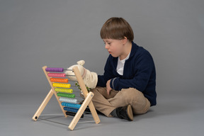 Kleiner junge, der neben einem zählspielzeug sitzt, während er eine puppe hält