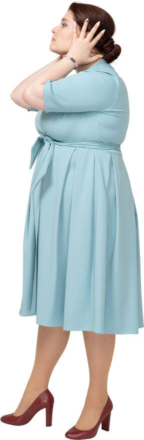 一个穿着蓝色连衣裙的女人用手捂住耳朵的侧视图