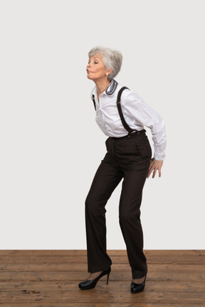 Three-quarter view of a squatting pouting old lady in office clothing