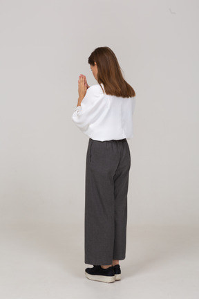 Three-quarter back view of a praying young lady in office clothing holding hands together