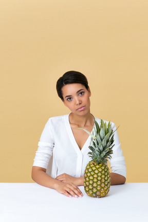 Девушка в белом платье сидит за столом с ананасом на нем