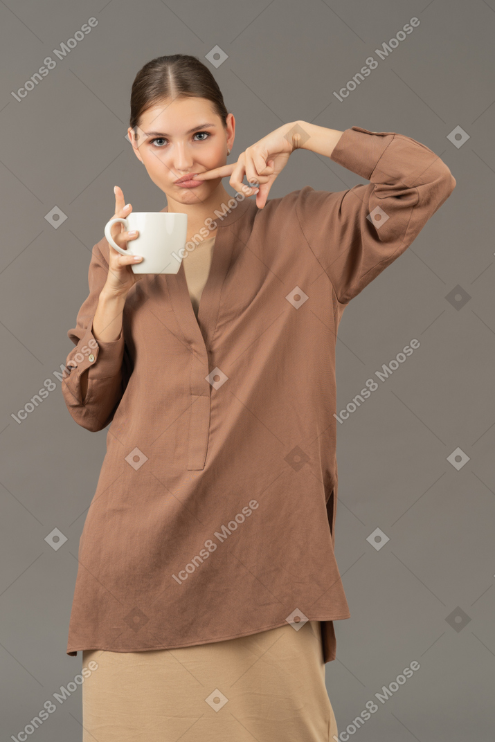 Frau hält eine tasse und steckt sich den finger in den mund
