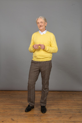 Front view an old smiling man wearing yellow pullover and putting hands together and looking at camera