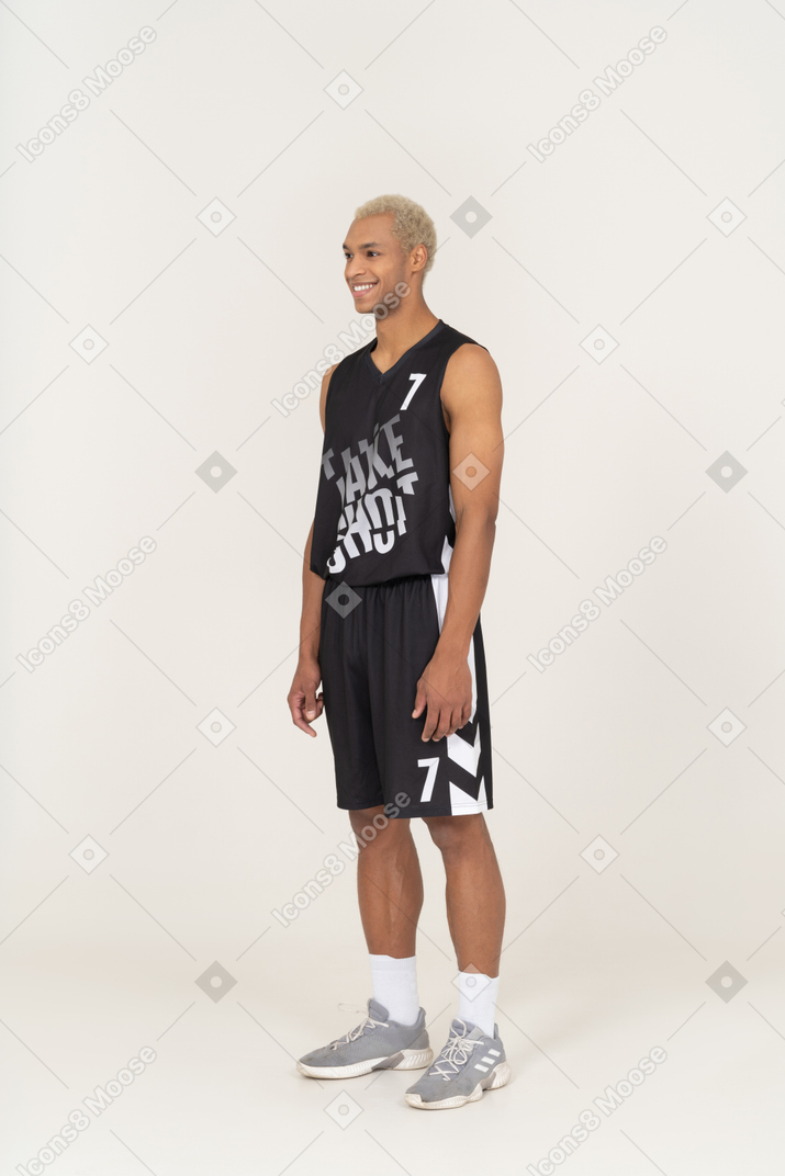 Vista di tre quarti di un giovane giocatore di basket maschile sorridente in piedi immobile