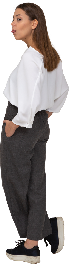 Vista posteriore di tre quarti di una giovane donna in abiti da ufficio che mette le mani in tasca e mostra la lingua