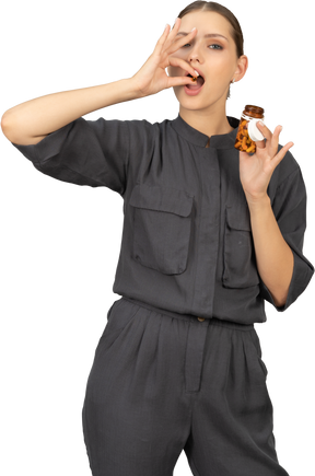 Vue de face d'une jeune femme en combinaison prenant des pilules dans un bocal