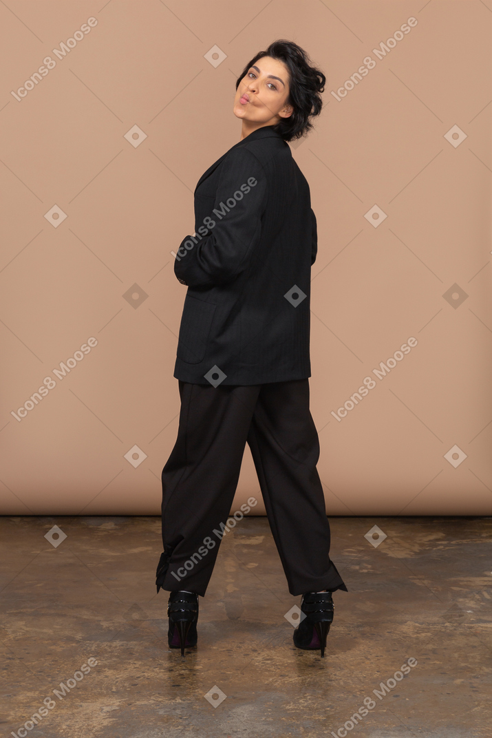 Back view of a businesswoman in a black suit pouting and looking at camera