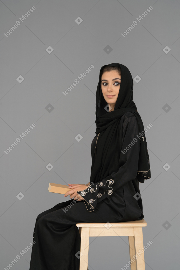 A covered arab woman holding a book on her knees