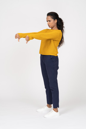 Vista lateral de una niña en ropa casual mostrando los pulgares hacia abajo