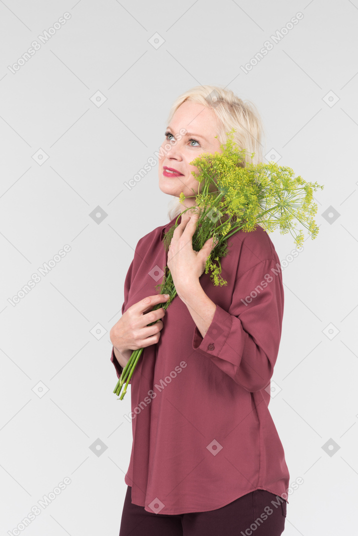 A nice-looking middle-aged blonde woman in a burgundy shirt and with a simple bouquet of flowers in her hands