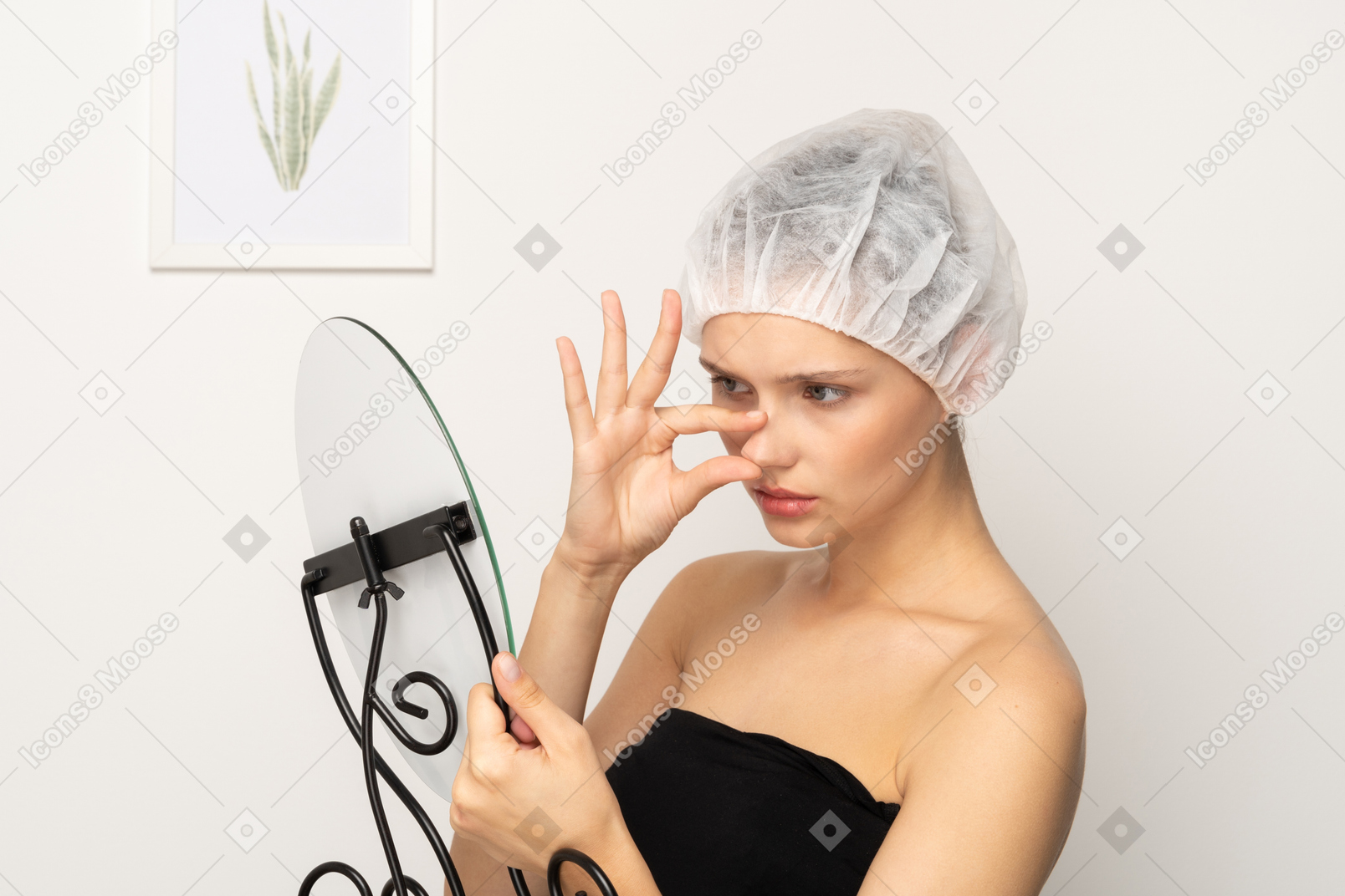 Unhappy young woman in medical cap looking in the mirror and touching her nose