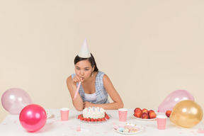 Jovem menina asiática sentado à mesa de aniversário e assobiando