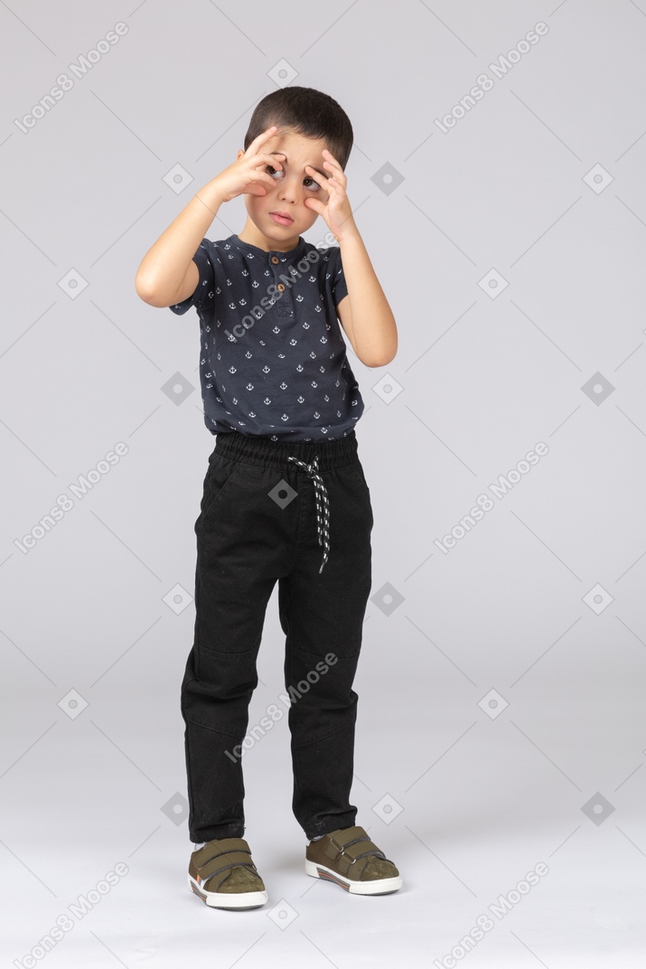 一个穿着休闲服的可爱男孩的前视图，透过手指看