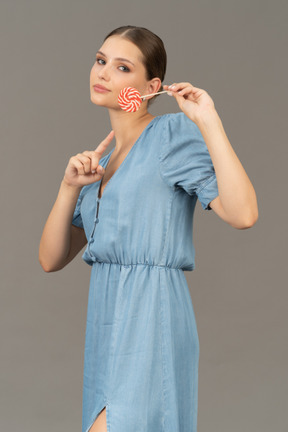 Three-quarter view of a young woman in blue dress holding a lollipop