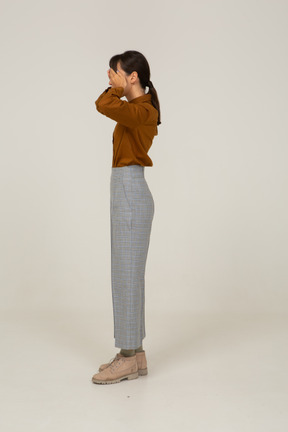 Side view of a young asian female in breeches and blouse hiding eyes