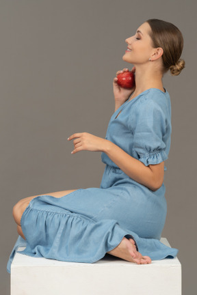 Side view of young woman with apple sitting on cube