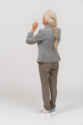 Вид сзади старушки в костюме, указывающей пальцами