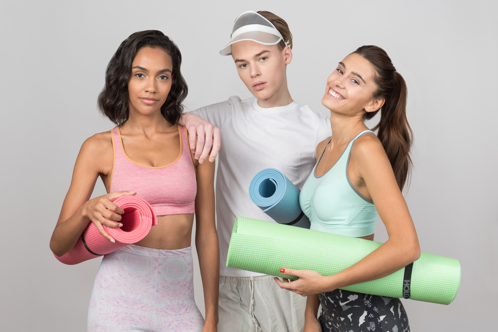 Two smiling young girls and guy holding yoga mats