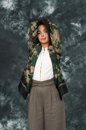 Modelo feminina em jaqueta de seda estampada com flores de mãos dadas atrás da cabeça