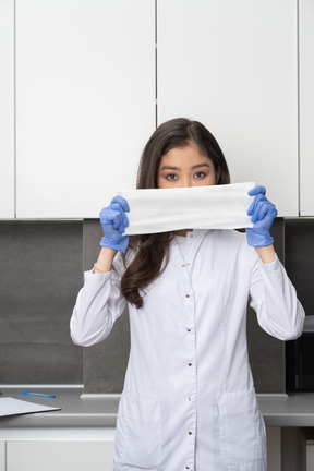 Vue de face d'une jeune femme médecin tenant un chiffon dans des gants de protection et regardant la caméra