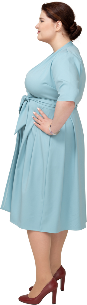 Vista lateral de uma mulher de vestido azul posando com as mãos na cintura