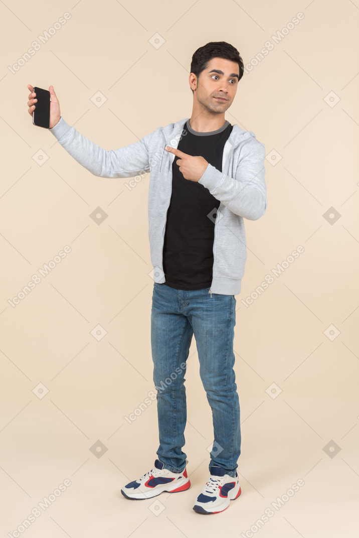 Jovem homem caucasiano apontando para smartphone que ele está segurando