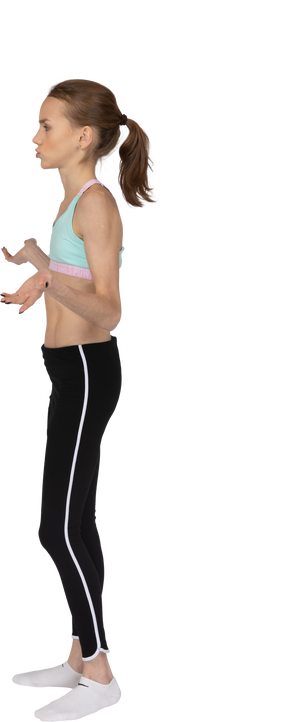 Vista lateral de una perpleja jovencita en ropa deportiva levantando las manos